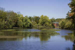 Fall foliage is reflected in the water at Delaware and Raritan Canal State Park in Princeton, New Jersey. An old red mill house can be seen in the background.